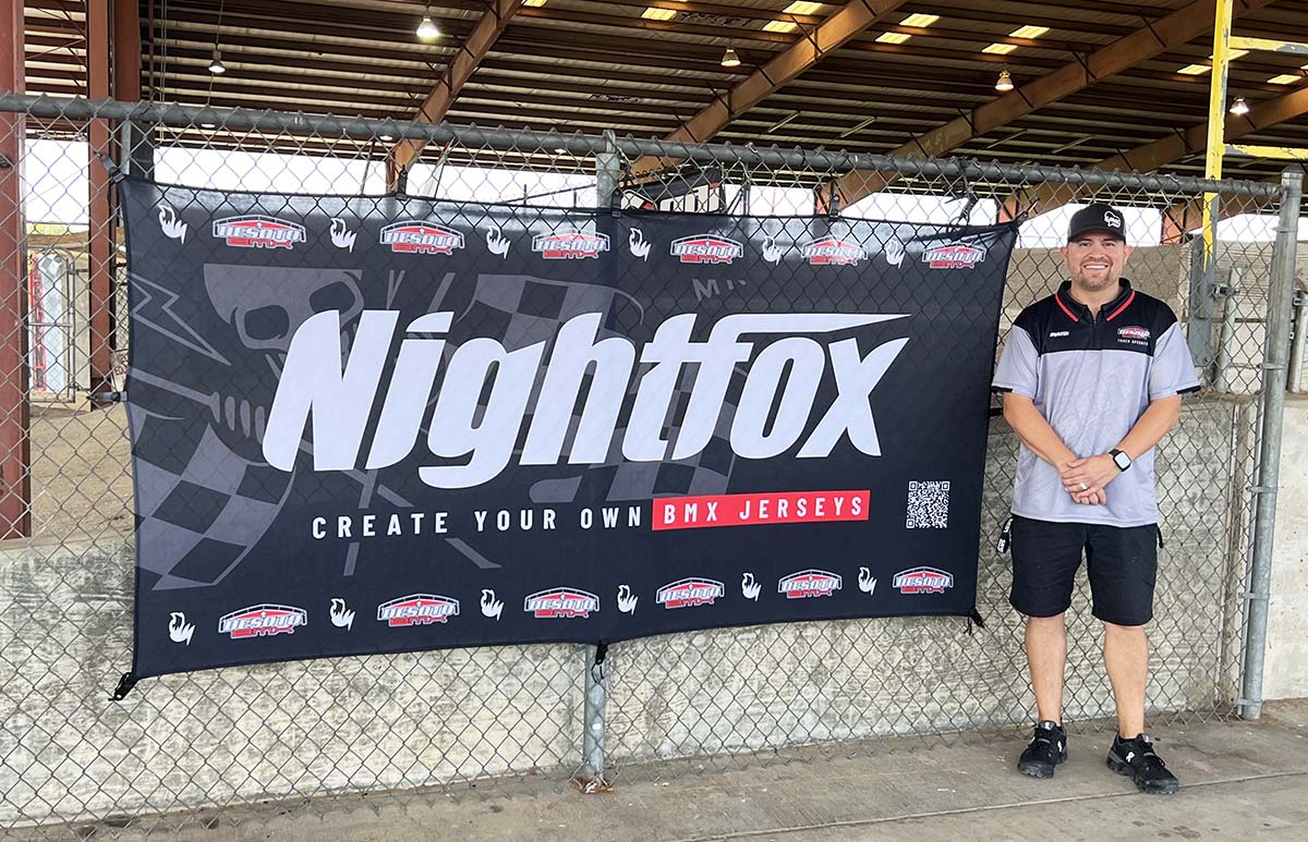 Bobby, the track operator of DeSoto BMX Track, standing near a Nightfox flag, proudly overseeing the track.