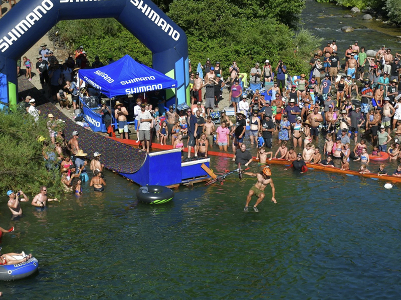 Riders from the Downieville Downhill Classic Race relaxing and diving into the lake after the event, with bikes resting nearby.