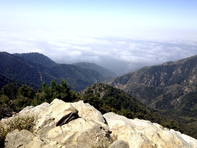 A mountain biker stops along the Mt. Wilson Trail, taking in the stunning view of the San Gabriel Mountains and surrounding valleys.