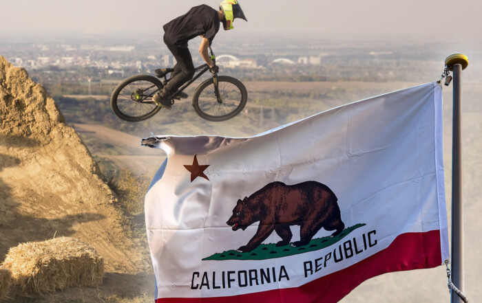 A mountain biker riding on a California trail with the California state flag prominently displayed in the foreground.