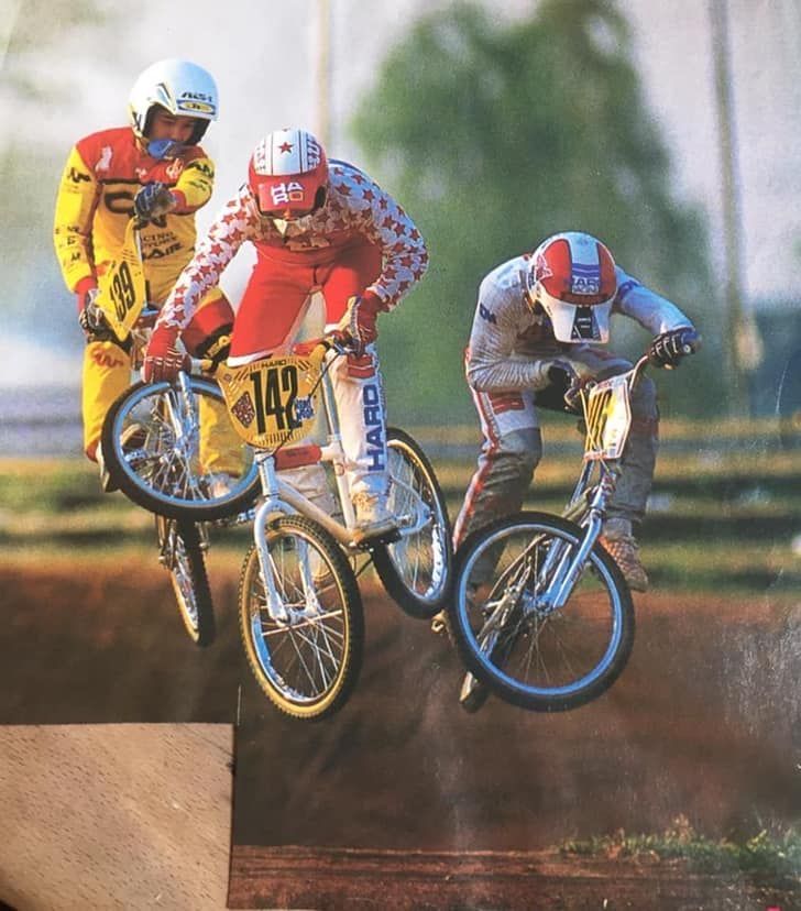 BMX riders from the 70s-80s racing in colorful jerseys, old-school BMX pants, and helmets.