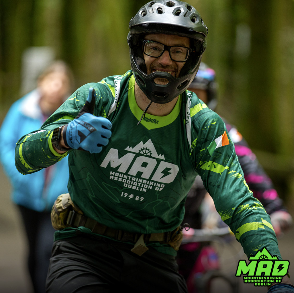 Team MAD MTB rider racing on trails, wearing the green version of their custom jersey with abstract patterns and personalized details.